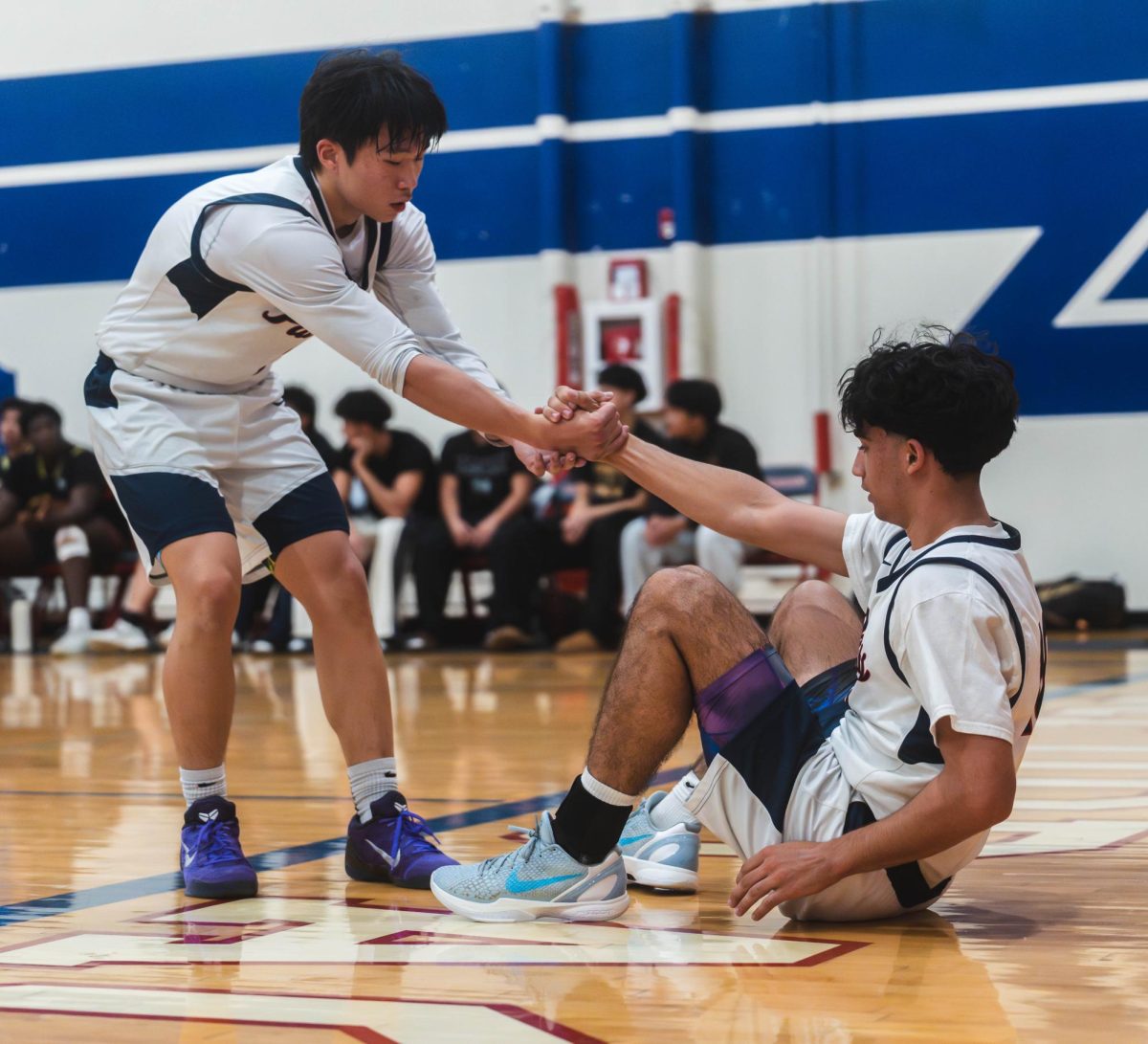 CAPTAIN COMRADERIE: Senior Varsity boys basketball captain David Jung helps up senior captain Colin Das.